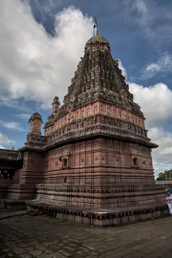 The carved stone spire of a Jyotirlinga temple against a cloudy sky