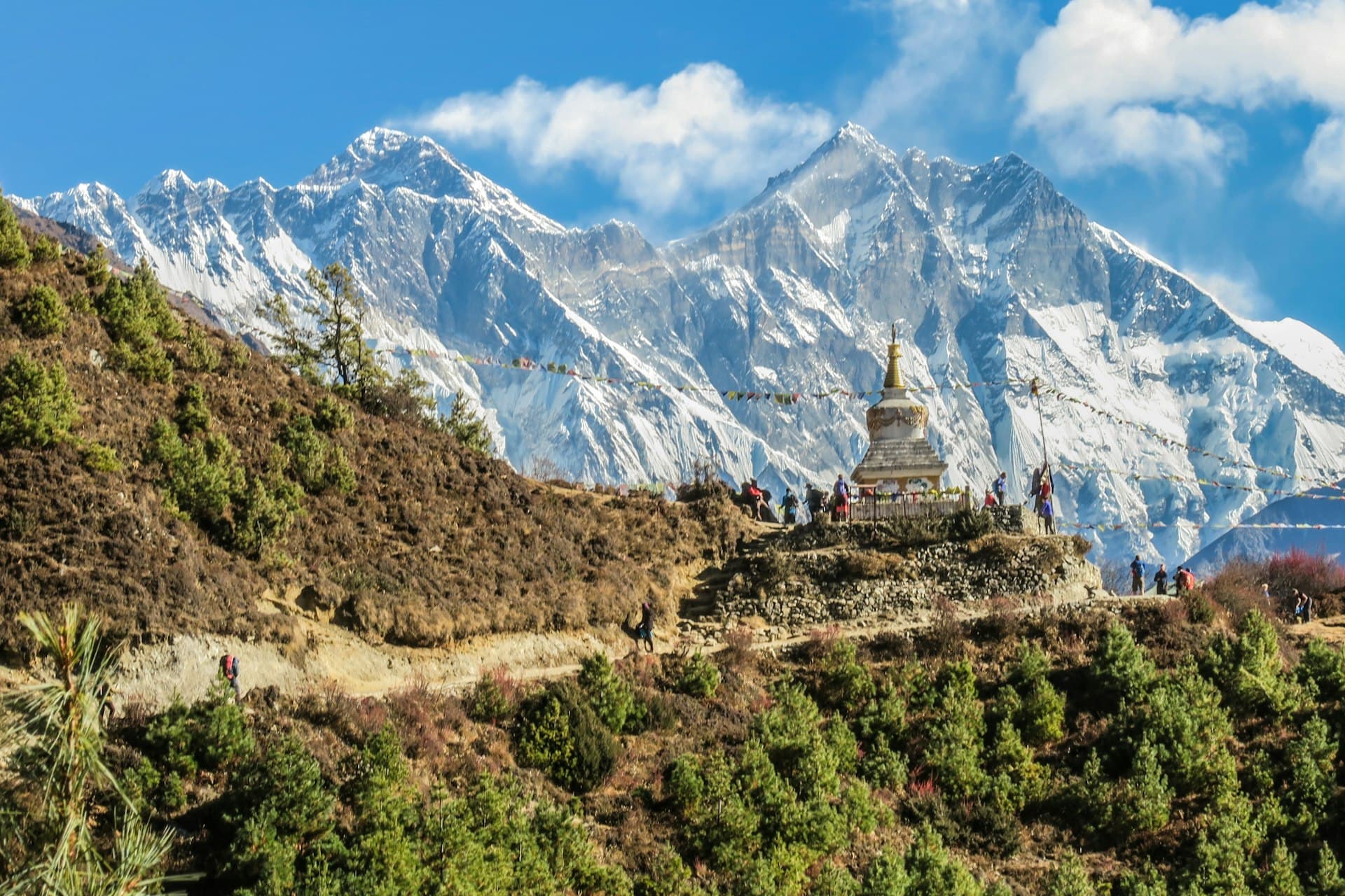 Hillside trail past a white stupa with Himalayan peaks behind